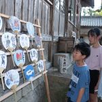 小学生たちがデザインしたうちわを眺める参拝客