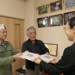 手作りの図鑑を野口館長に手渡す小林さん（左）と佐古さん