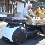 中型の自動配送ロボットに野菜を積み込む地元住民