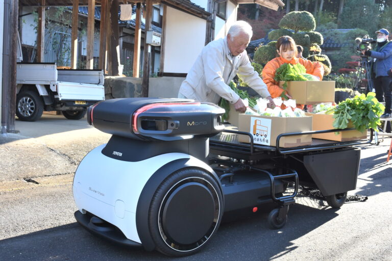 中型の自動配送ロボットに野菜を積み込む地元住民