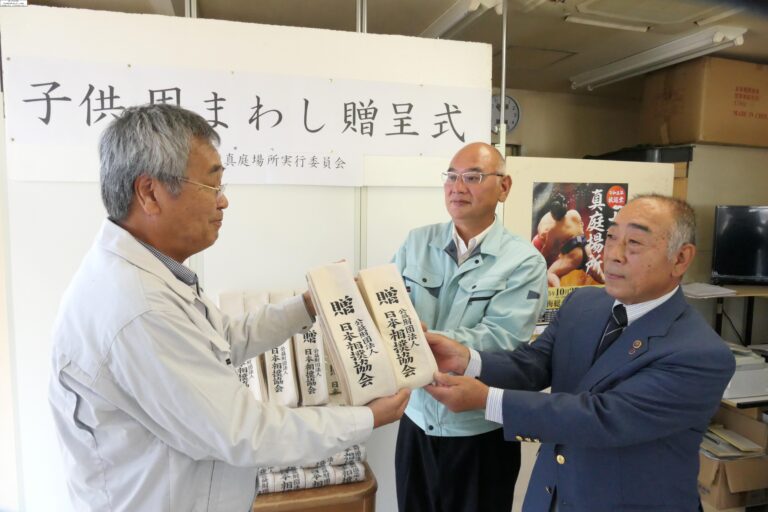 まわしを受け取る真庭市スポーツ協会相撲部の村上部長（右）と湯浅監督（中央）=岡山県真庭市で