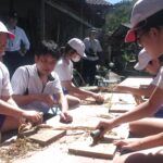 上田さんに教わりながらミツマタをへぐる子どもたち=岡山県津山市で