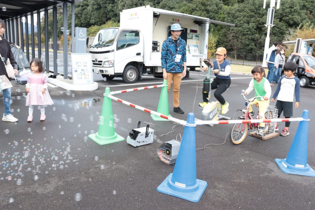 自転車型の人力発電機のペダルをこぐ子ども