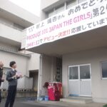 村上さんのデビューを祝う横断幕を見上げる町職員ら=岡山県美咲町で