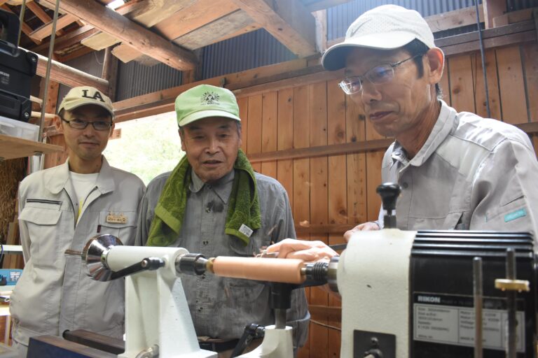 木製シャープペンシルを1本1本、手作りする田中理事長（左）ら=岡山県津山市=