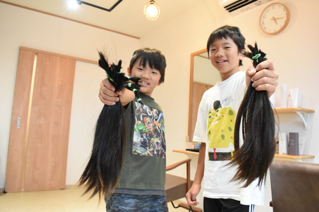 切った髪の束を手にする兄弟