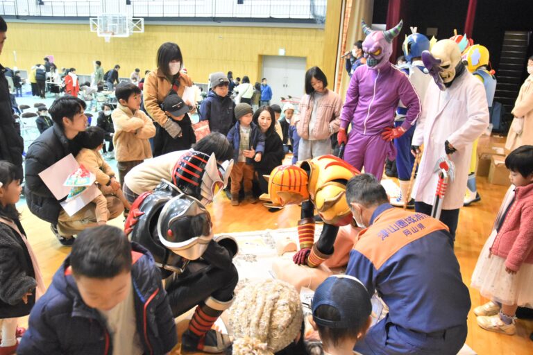 ヒーローと一緒に心肺蘇生に挑戦する参加者=岡山県津山市で