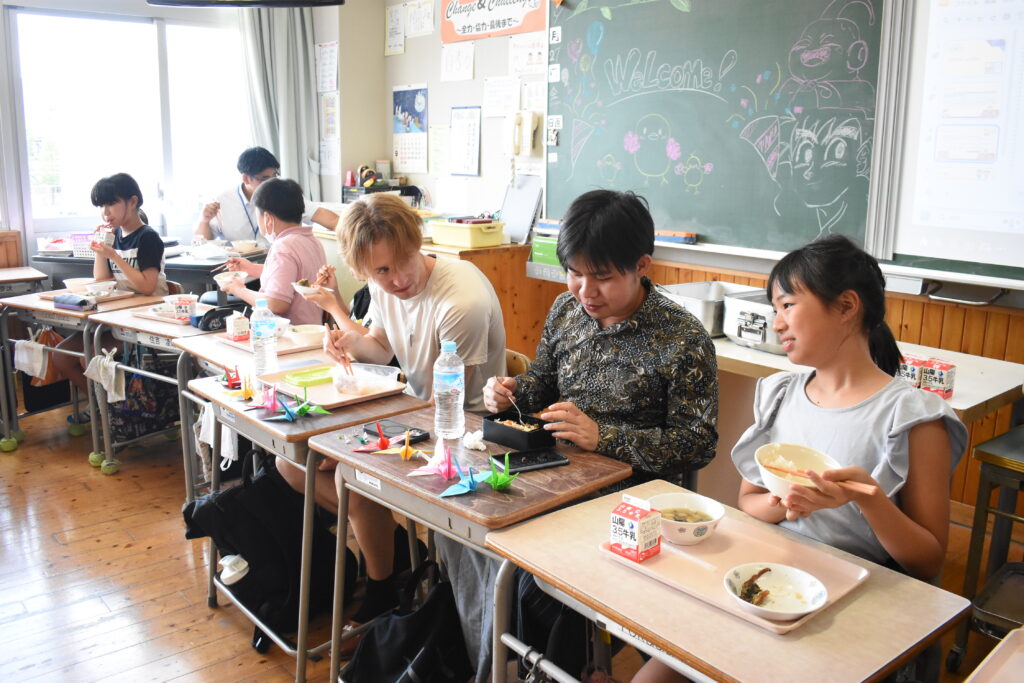 一緒に昼食を味わう留学生と児童