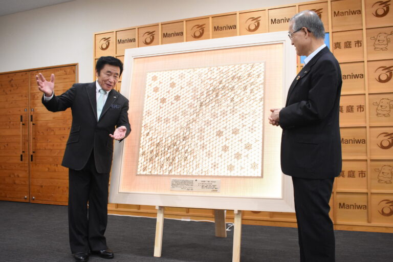 寄贈した「真庭組子」の額装「極」について説明する佐田建美の佐田社長（左）＝岡山県真庭市で