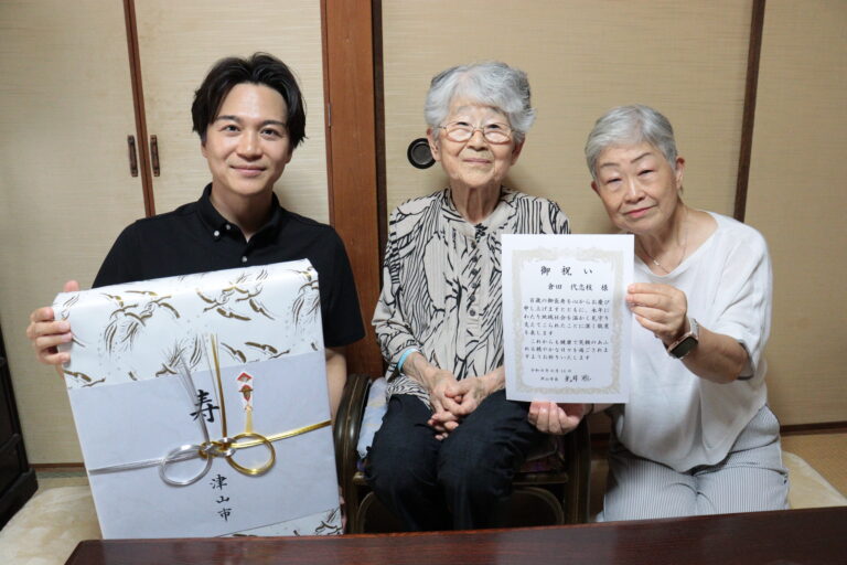 次女の河原さん（右）と光井市長（左）から祝福を受ける倉田さん＝岡山県津山市で