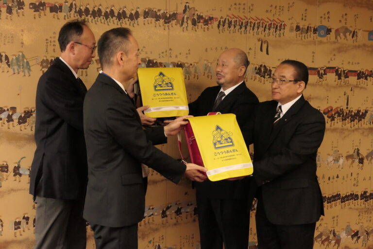ランドセルカバーを寄贈する石本支部長（右から二番目）と番原理事長（右）=岡山県津山市で