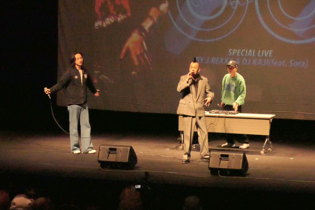 主題歌「53号線」を歌うJｰREXXXさん（中央）ら