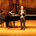 加藤さんの演奏に合わせて美しい歌声を響かせる小峪さん＝岡山県津山市で