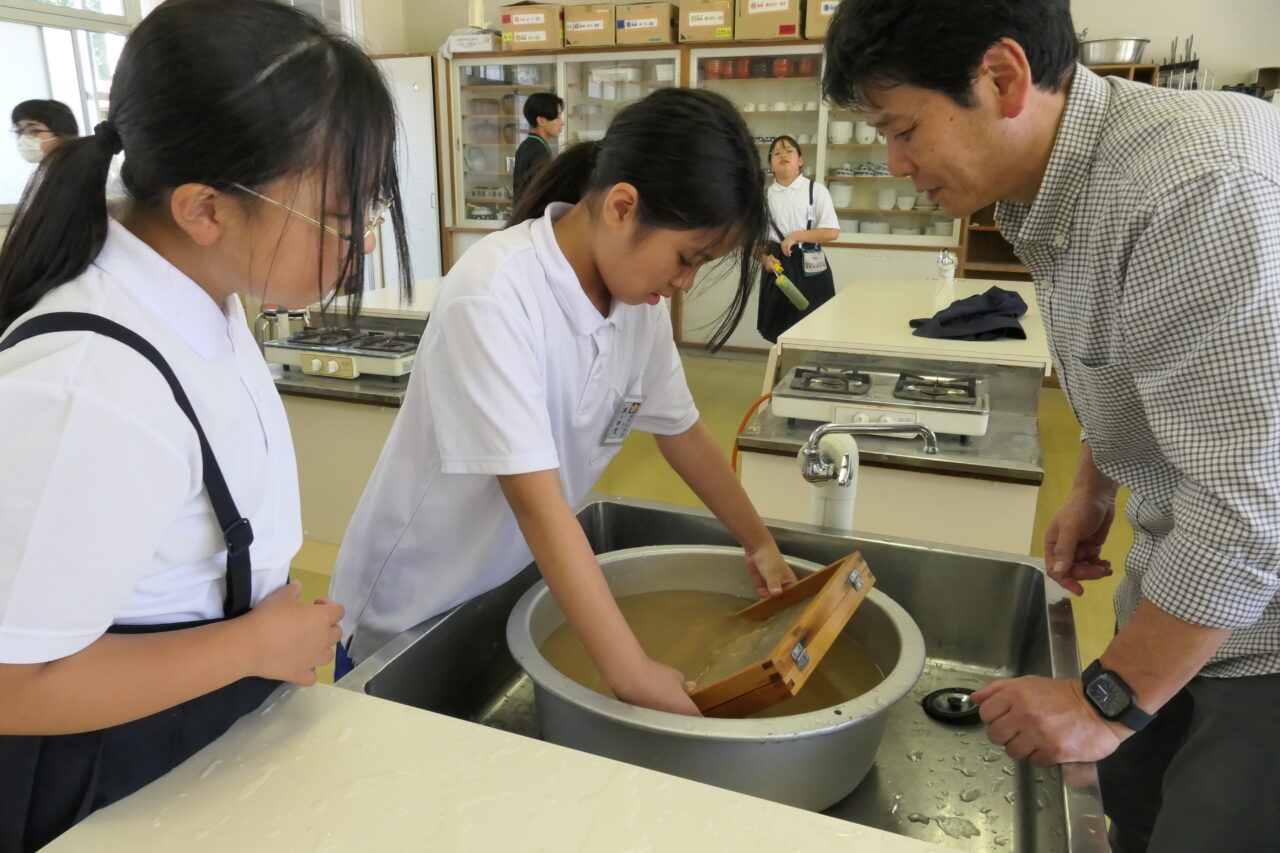 上田さんに教わりながら紙すきを体験する児童=岡山県津山市で