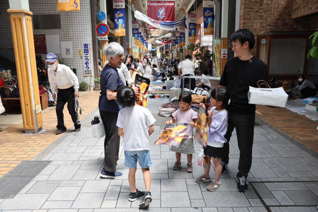 商店街でポスターを配布し上映をPRするファンら