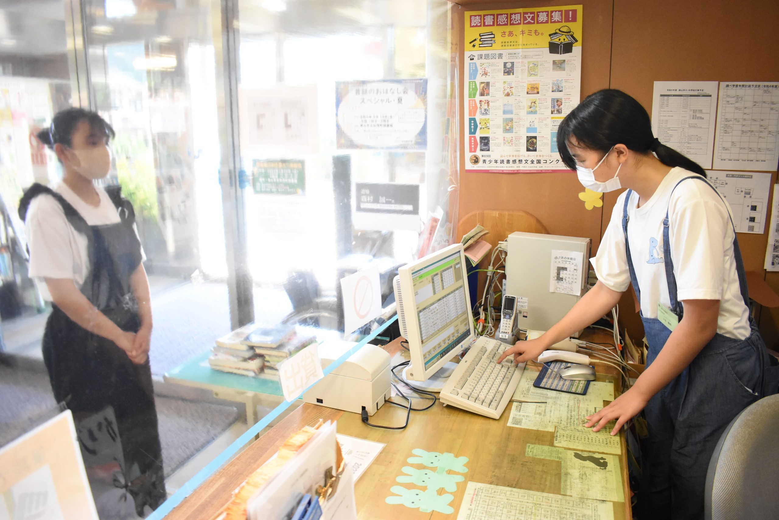 窓口で本の貸し出し業務を体験する上谷さん（右）＝岡山県津山市＝