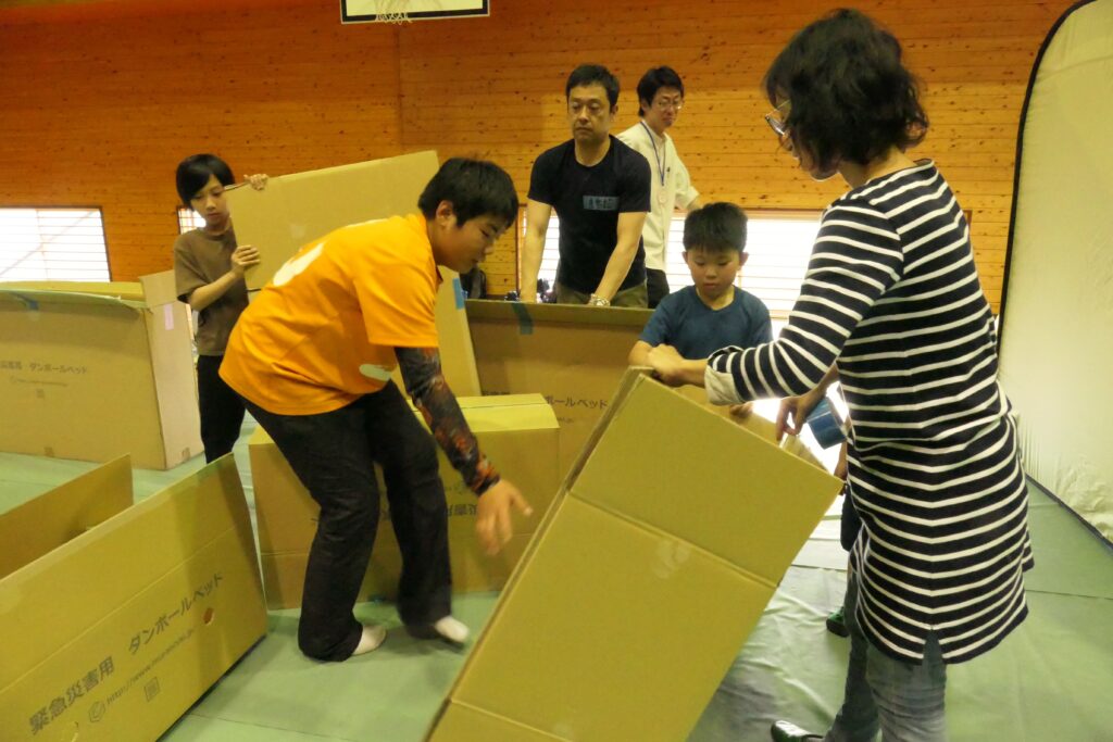 教わりながら簡易ベッドを組み立てる子どもたち