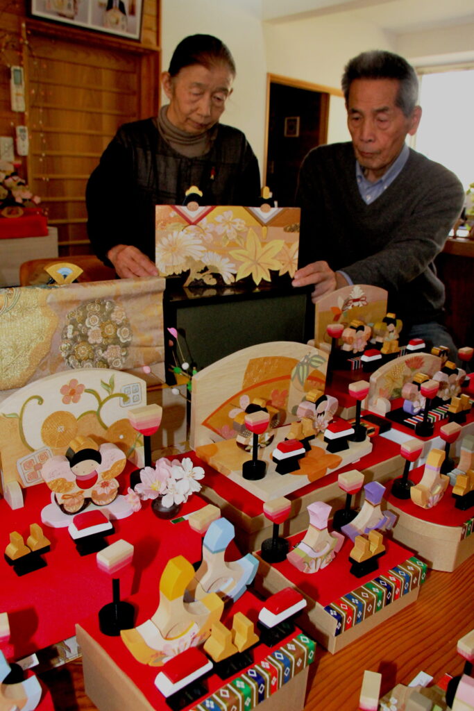 一枚板の夫婦びなを手にする藤原さん夫妻