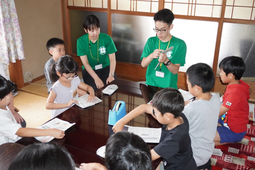 新聞紙で即席スリッパを作る子どもたち