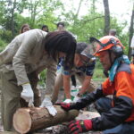 丸太の樹皮はがしを体験する友納環境大臣政務官＝岡山県真庭市で