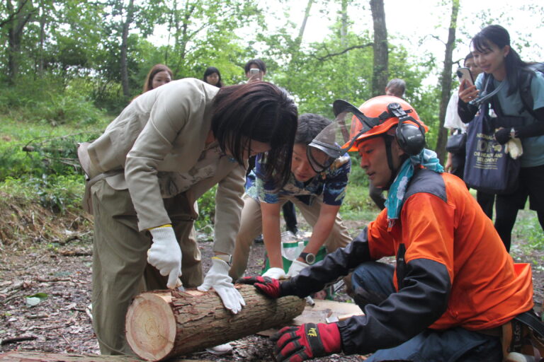 丸太の樹皮はがしを体験する友納環境大臣政務官＝岡山県真庭市で