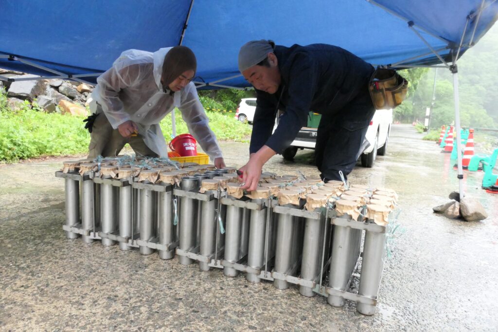雨の中、テントの下で準備を進める花火師