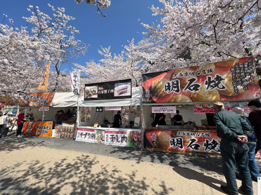 桜で囲まれたご当地グルメのブース　津山城三の丸つるやま広場