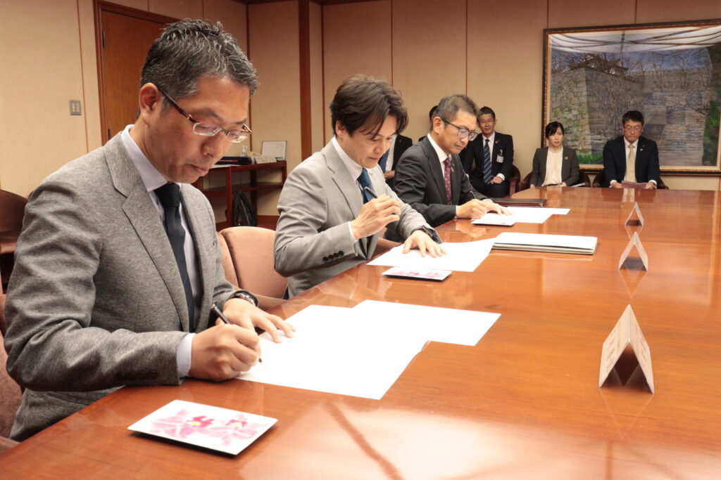 協定書に署名する下村社長(左)光井市長(中央)、山縣代表取締役