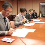 協定書に署名する下村社長（左）光井市長（中央）、山縣代表取締役