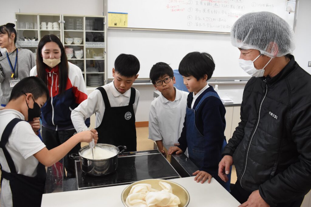 早瀬久善さん（右）に教わりながら豆富作りに励む児童たち