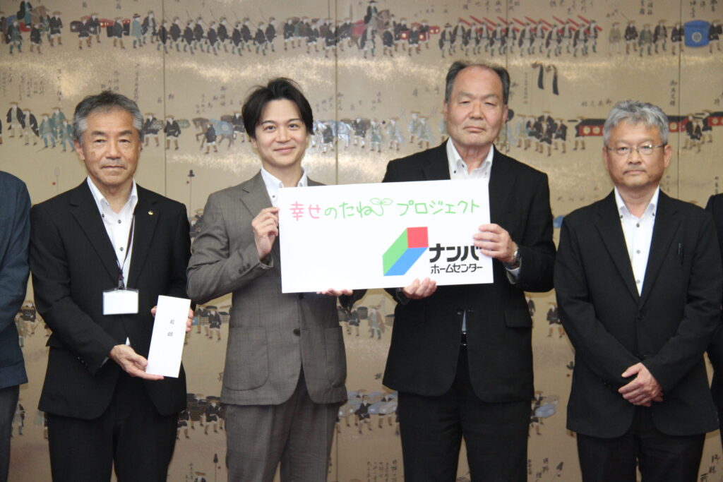 総額74万円分のクーポン券の目録を手にする(左から)光井聡市長、ナンバホームセンターの江見幸敏管理本部長、同社関係者